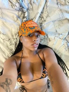 a woman laying on top of a bed wearing an orange and black hat with tattoos