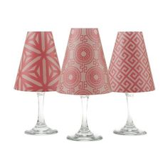 three wine glasses sitting next to each other on top of a white surface with red and pink lampshades