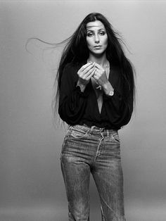 a black and white photo of a woman with long hair wearing jeans, holding her hands together