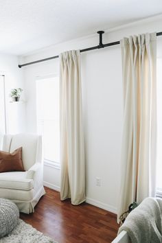 a living room with white furniture and wood flooring is pictured in this image, the curtains are open