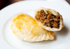 two pastries sitting on top of a white plate with meat and cheese in the middle