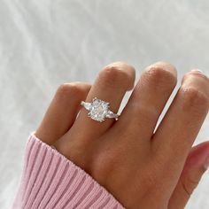 a woman's hand with a diamond ring on her left hand and a pink sweater on the right