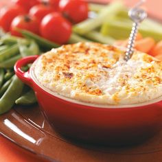 a red dish filled with food next to green beans and carrots on a plate