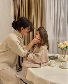 two women are sitting at a table and one is touching the other's face