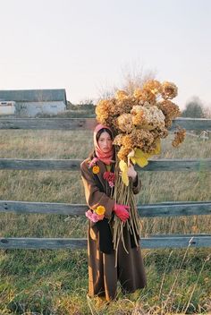 a woman is standing in the grass with flowers on her head and holding onto a fence