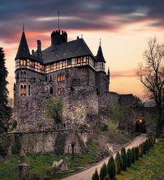 an old castle lit up at night with the sun going down on it's roof