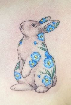 a rabbit tattoo with blue flowers on its back shoulder and chest, sitting in front of the viewer