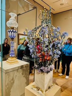 people are looking at some art on display in a glass walled room with blue and white vases