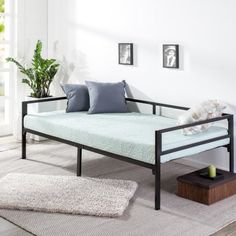 a day bed sitting on top of a wooden floor next to a potted plant