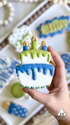 a hand holding up a decorated cookie in the shape of a birthday cake