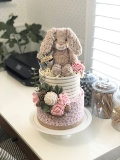 a three tiered cake decorated with flowers and a stuffed bunny on top is sitting on a table