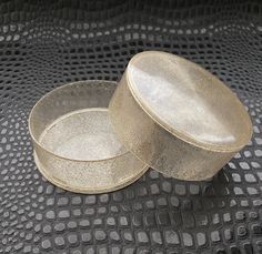 two round metal containers sitting on top of a black table covered in silver circles and dots