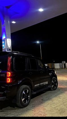 a black suv is parked in front of a gas station at night with its lights on