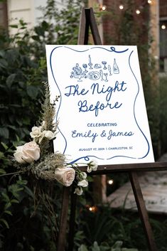 a sign with flowers on it sitting in front of some bushes and trees at night