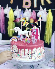 a birthday cake decorated with unicorns and rainbow streamers is being held by a child's hand