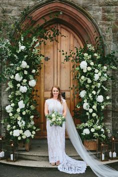 a woman standing in front of a doorway with flowers and greenery on the side