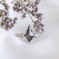 a diamond ring sitting on top of a white cloth next to some purple and white flowers