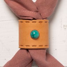 a brown leather cuff with a turquoise stone in the center on a pink scarf against a white brick wall