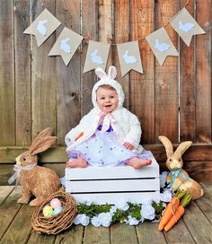 a baby is sitting on a crate surrounded by bunnies and carrots, while wearing bunny ears