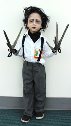 a young boy with scissors in his hands and hair on top of his head, standing next to a wall