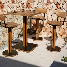 two wooden chairs and a table in front of a stone wall with rocks on it