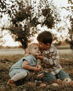 two young children sitting in the grass with apples on their hands and looking at each other