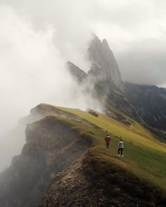 two people are walking up the side of a mountain on a foggy day with mountains in the background