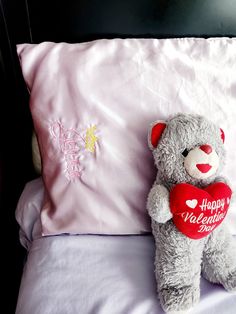 a gray teddy bear sitting on top of a bed next to a pillow with a happy valentine's day message