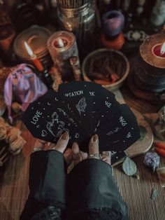 a person holding four cards in their hands with candles and other items around them on the table