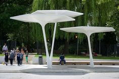 people are walking around in the park near large white structures with trees and bushes behind them