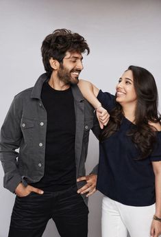 a man and woman smile at each other as they pose for a photo in front of a gray background