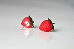 two red strawberry shaped studs with green leaves on each side and a pin in the middle