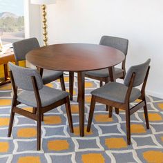 a dining room table with four chairs in front of a window and a rug on the floor