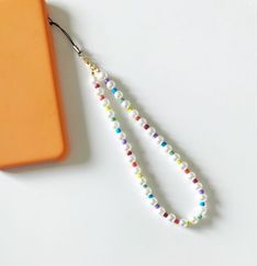 a white beaded lanyard with an orange case on the table next to it