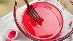 a whisk is being mixed in a bowl with red powder and a measuring cup