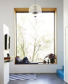 a person sitting on a window sill in front of a large window with a tree outside