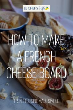 a wooden cutting board topped with cheeses and fruit on top of a white table