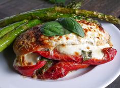 a white plate topped with a sandwich covered in cheese and sauce next to asparagus