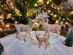 two deer figurines are standing in the snow next to christmas trees and lights