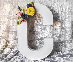 the letter g is decorated with flowers on it's side and sits next to a curtain