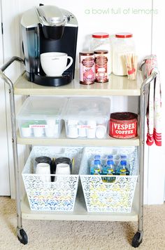 a kitchen cart with two baskets on it and coffee maker next to it, in front of a white wall