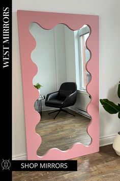 a pink mirror sitting on top of a wooden floor next to a potted plant