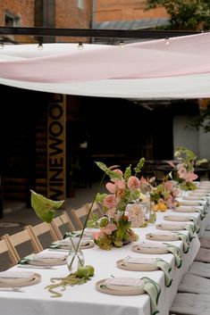 a long table is set up with flowers and place settings for dinner guests to sit at