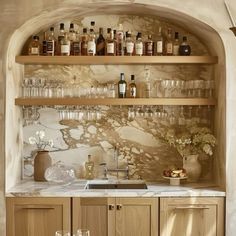 a kitchen filled with lots of bottles and glasses on top of a wooden shelf next to a sink