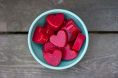 a blue bowl filled with red heart shaped gummy bears on top of a wooden table