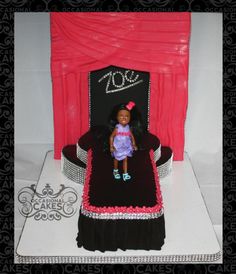 a doll sitting on top of a black chair in front of a red stage curtain