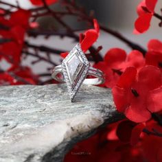 a diamond ring sitting on top of a rock with red flowers in front of it