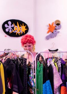 a woman with red hair standing in front of a rack of clothes