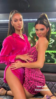 two beautiful women in pink dresses posing for the camera with one woman's legs crossed