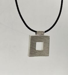 This geometric pendant has a square shape with a smaller square cutout in the center, giving it a modern and minimalist look. It is made of 925 sterling silver. Its finish is rough which gives it an industrial look. The pendant is strung on black silk cord with a handmade hook clasp. This necklace is perfect for everyday wear or as a statement piece for special occasions. DESCRIPTIONS and MEASUREMENTS: Materials: Sterling silver 925. Dimensions: 2,7x2,2 (cm) 1,06x0,87 (in)" thickness 0,5 (cm) 0, Minimalist Geometric Jewelry, Necklaces Geometric, Industrial Jewelry, Industrial Pendant, Silk Cord, Necklace Minimalist, Square Pendant, Modern Necklaces, Geometric Pendant